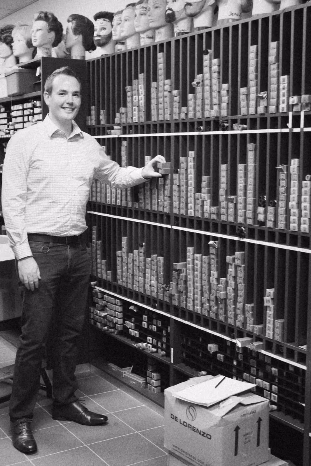 Ben smiling beside the floor to ceiling colour wall at Toowoomba TAFE, training heads lined up along the top shelf