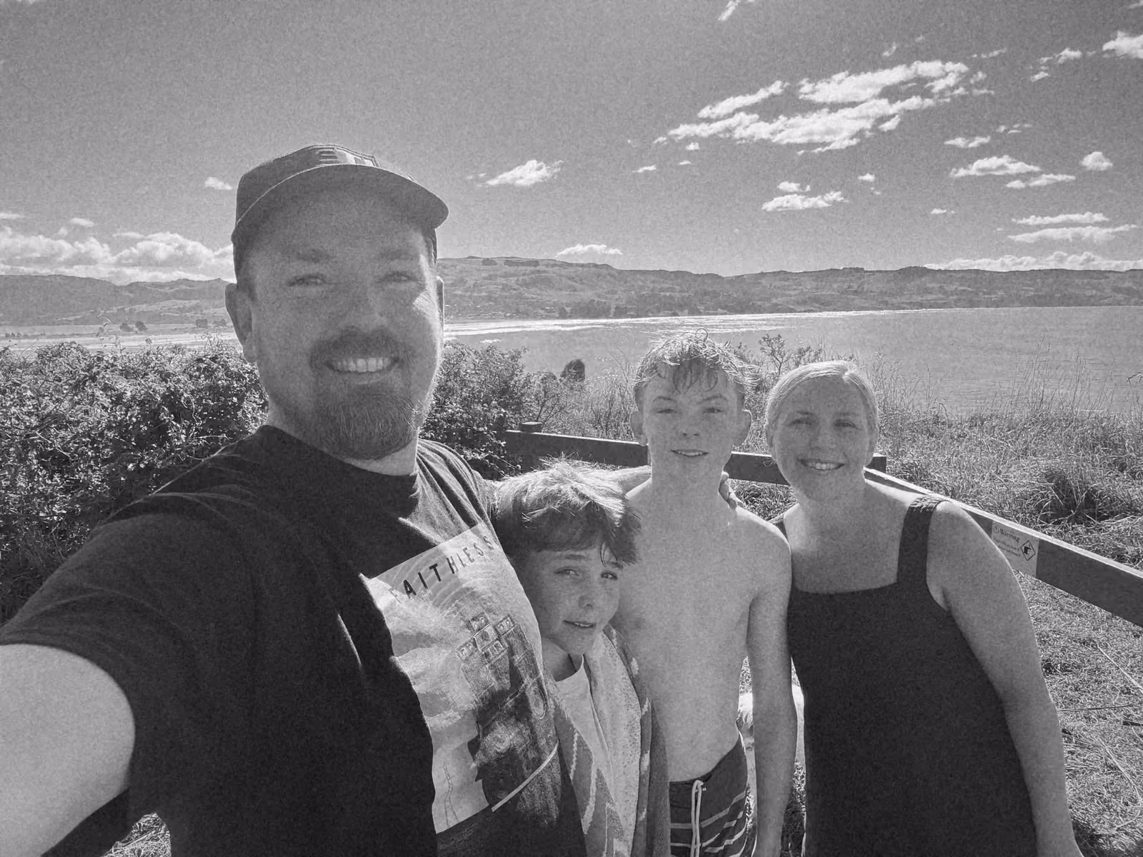 Ben taking a selfie with his family on a clifftop above a beach and green hills