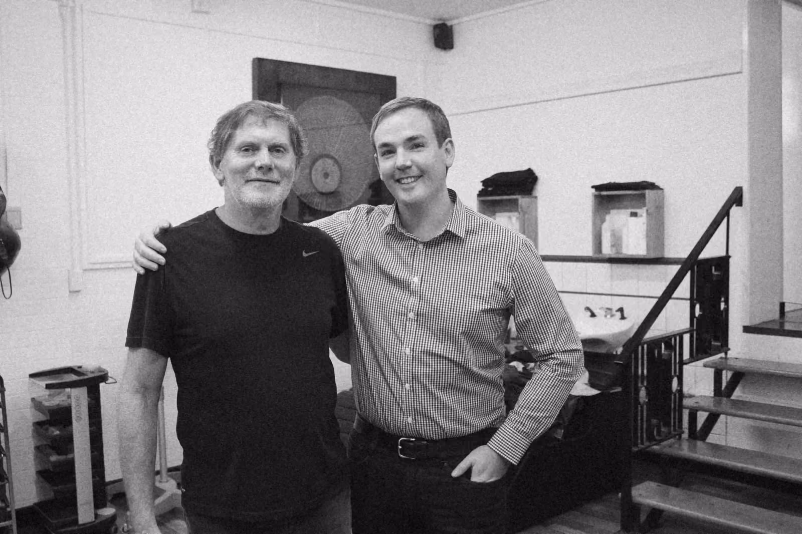 Ben with his arm around a hairdresser in a salon, a backwash basin behind them