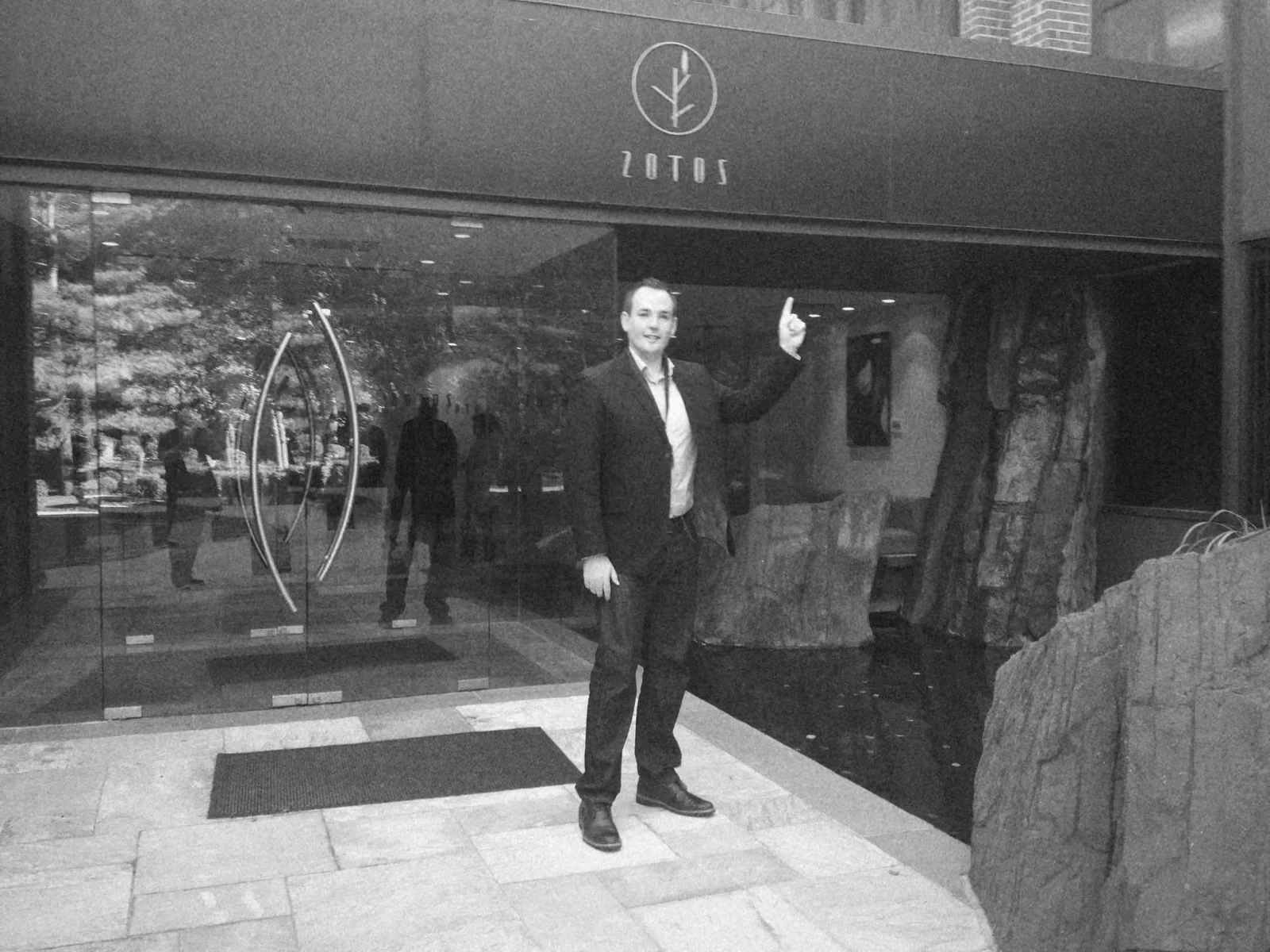 Ben pointing up at the Zotos sign above the glass doors of its head office