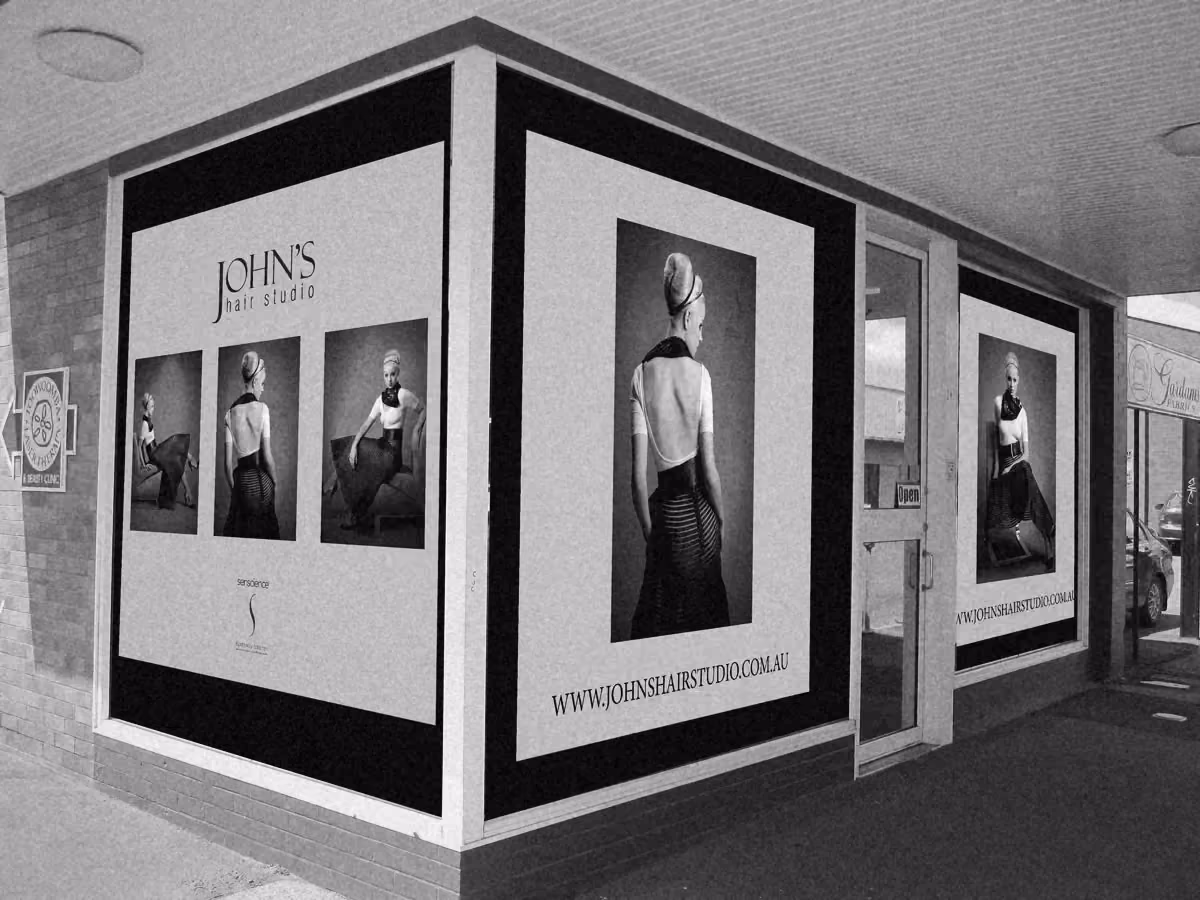 A mockup of black and white window posters on the corner shopfront of John’s Hair Studio