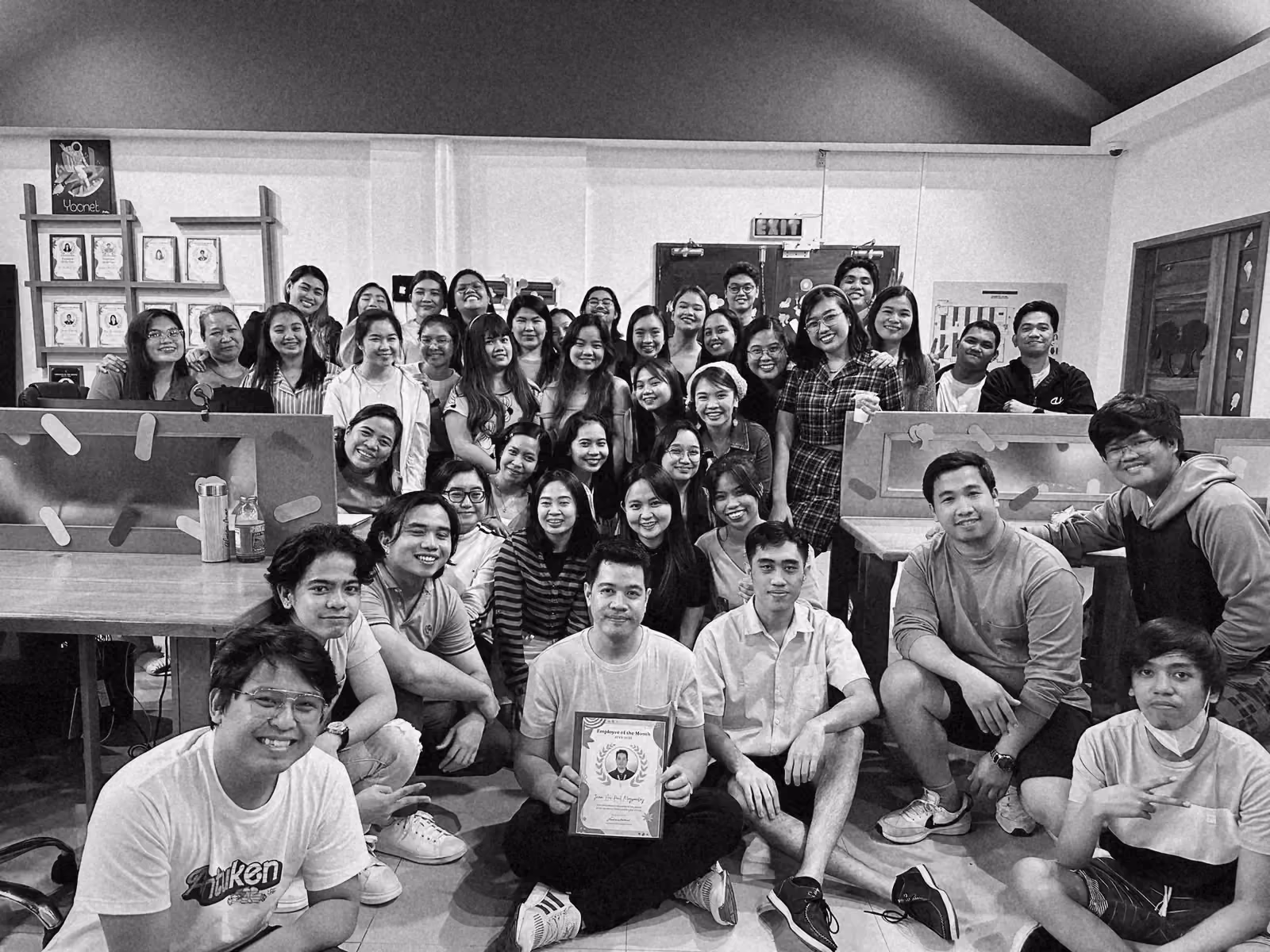 The team gathered in front of the desks, a framed certificate held up in the front row