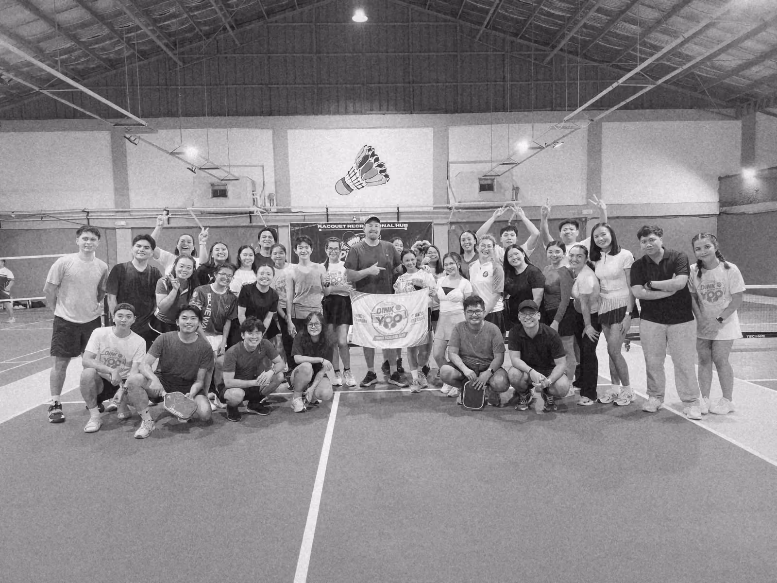 The team on a blue indoor court holding up the club flag