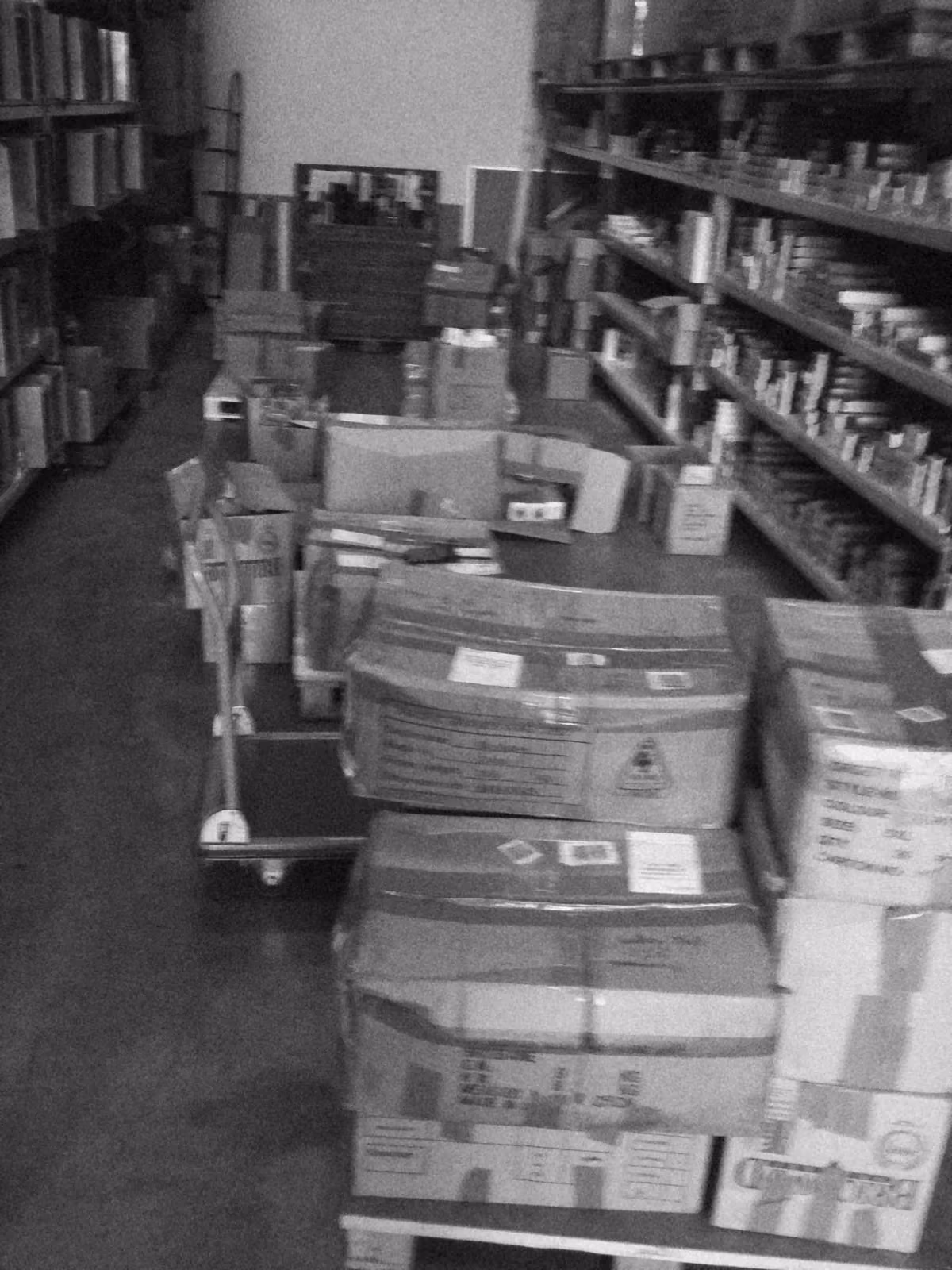 Cartons and pallets of stock stacked down a warehouse aisle between shelves of product